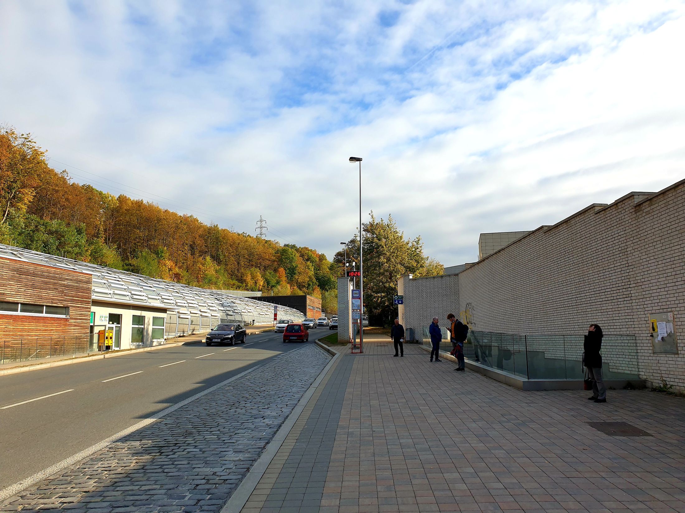 Vlevo stanice metra Nemocnice Motol - vchod z ulice, vpravo zastávka autobusu Nemocnice Motol, vchod do podchodu a protihluková stěna